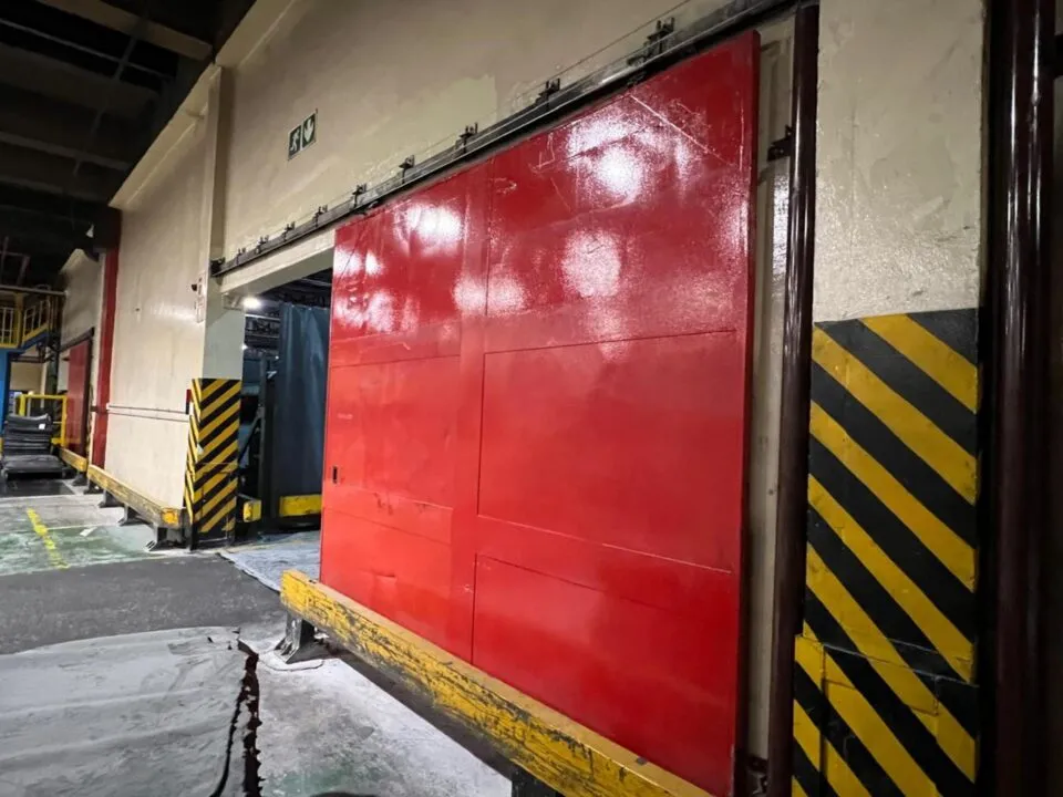 Red sliding door beside yellow-and-black safety markings in a warehouse
